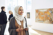 Portrait of a muslim woman of african nationality, art academy student at a contemporary exhibition at the museum of contemporary art. In the background abstract paintings and people, gallery visitors