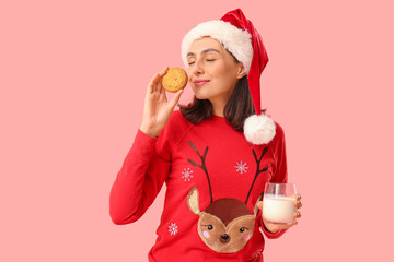 Poster - Beautiful happy young woman in Santa hat with cookie and glass of milk on pink background