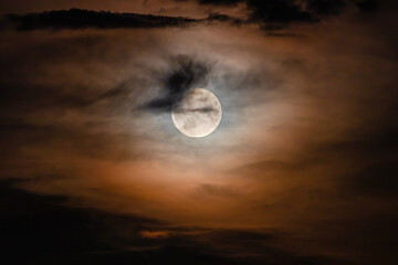 Wall Mural - Full moon on a cloudy night. Natural colored clouds around the Moon in the sky are an optical effect caused by the refraction of moonlight from ice crystals in the upper atmosphere
