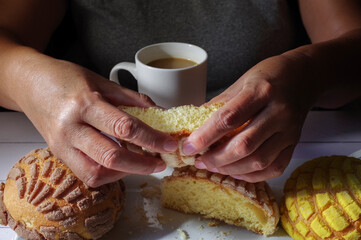 Wall Mural - Hands of Mexican Hispanic woman. Concept of taking food with hands or handling food. cuting a Mexican sweet bread with two hands on a white plate and a cup of coffee horizontal