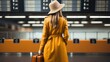 A woman traveler in a yellow raincoat with a backpack stands at the airport and looks for the board of her flight Information