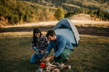 Two people camp on a hill, cooking and enjoying the view of a distant lake