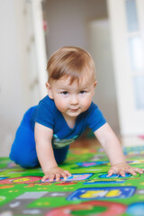 Wall Mural - Baby boy crawls on the home floor and looking at camera. Front view. Kids innocence. Love and family emotion