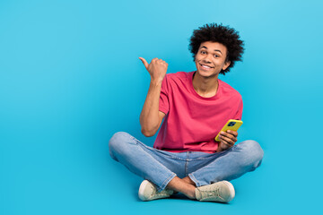 Full size photo of attractive young man point empty space hold telephone wear trendy pink clothes isolated on blue color background