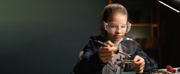 Cute girl in safety glasses, learning how to solder microprocessor cables and printed circuits uses a magnifying glass, repairing electronics