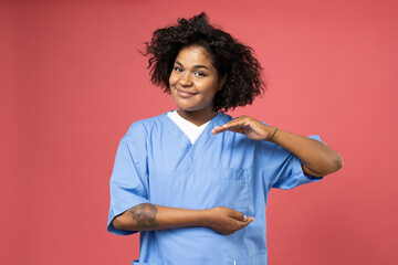Wall Mural - Smiling curly woman in doctor's clothes on pink background