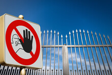 Closeup Of A No Trespassing Sign Or Do Not Enter Sign, And A Closed Gate (wrought Iron Gate With Sharp Points) Of A Private Property Against A Clear Blue Sky With Clouds And Copy Space.