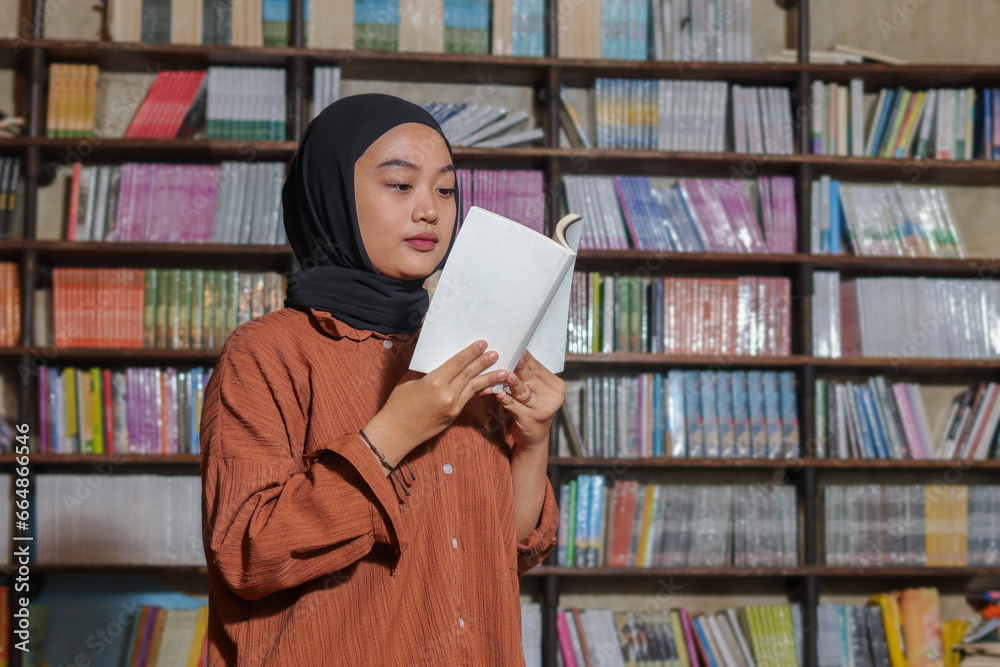 Portrait of Asian hijab woman holding book in front of library ...