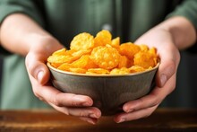 Hand Holding Cheese Puffs Over A Bowl