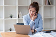 © wichayada - Attractive Asian woman using laptop in online meeting. Businesswoman using mobile phone talking with colleague sitting at table in modern office