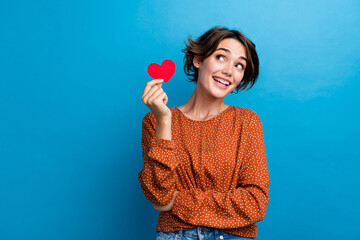 Poster - Photo portrait of pretty young girl hold little red heart look empty space wear trendy brown outfit isolated on blue color background