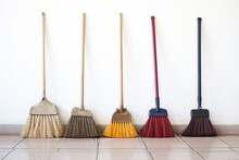Row Of Tall And Short Brooms Against A Clean Wall