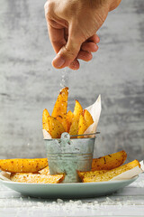 Canvas Print - A serving of baked potato wedges in a plate. Delicious vegetarian food. Hand salting a dish