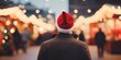 Rear view of a man wears red Santa hat walking in Christmas market decorated with holiday lights in the evening. Feeling happy in big city, generative ai