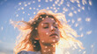 A young woman with blond hair and closed eyes stands against a blue sky. The woman's hair flutters in the wind and is illuminated by the sun. Around the woman's head there are numerous abstract lights
