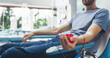© Gorodenkoff - Close Up Shot Of Hand Of Male Blood Donor With an Attached Catheter. Caucasian Man Squeezing Heart-Shaped Red Ball To Pump Blood Through The Tubing Into Bag. Donation For Heart Surgery Patients.