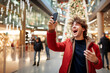 © PETR BABKIN - YOUNG ADULT MAN REJOICES AT A MESSAGE RECEIVED ON A SMARTPHONE IN A SHOPPING MALL. image created by legal AI