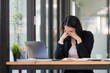 © Songsak C - A tired businesswoman under stress works at a laptop while sitting at a table at home and holds her hand on her temples, causing migraine attacks.