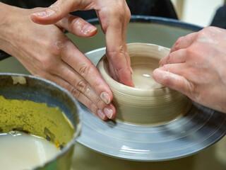 Close-up of people's hands making an object out of raw clay on a potter's wheel. Conducted master classes and workshops. Hobby, selective focus