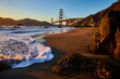 Gorgeous sunset striking Golden Gate Bridge from sandy beach with sea foam on shore