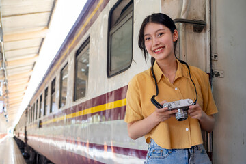 Asian teenage girl traveling using a camera take a photo to capture memories while waiting for a train at the station