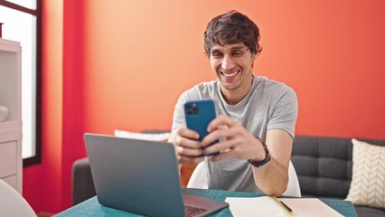 Wall Mural - Young hispanic man using smartphone smiling at dinning room