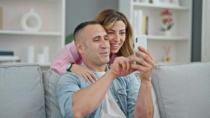 Canvas Print - Man and woman couple using smartphone sitting on sofa at home