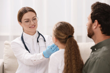 Canvas Print - Smiling doctor examining girl`s oral cavity near her father indoors