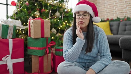 Canvas Print - Young hispanic woman sitting on the floor wearing christmas hat looking bored at home