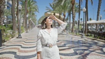 Wall Mural - Young beautiful hispanic woman covering eyes looking at the sun at city promenade