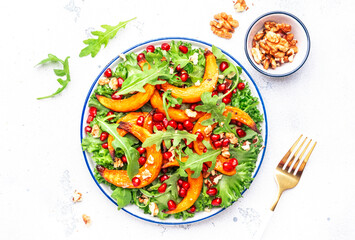 Wall Mural - Vegan autumn salad with baked sweet pumpkin, lettuce, arugula, pomegranate seeds and walnuts. Comfort slow  food. White table background. Top view