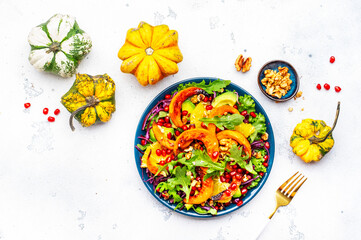 Wall Mural - Delicious vegan pumpkin salad with red cabbage, avocado, lettuce, arugula, pomegranate and walnuts. Autumn healthy eating, slow comfort food. White table background
