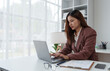 © Phimwilai - Asian businesswoman working with laptop financial documents Data recording Online communication at work desk in modern office.