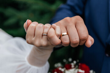 The intertwined fingers of the bride and groom, showing gold wedding rings on the background of the bouquet.