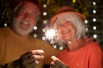 Wall Mural - Blurred caucasian senior couple holding sparklers celebrating new year. Happy lifestyle for mature retirees, party lights