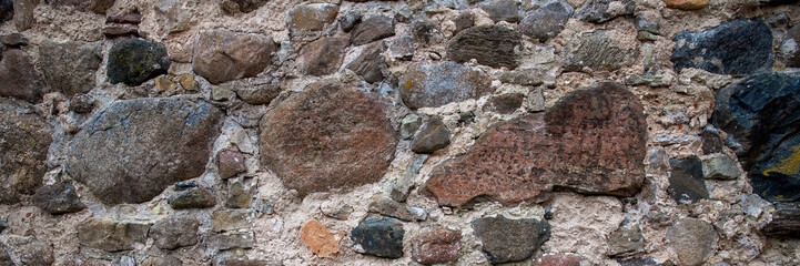 Ancient stone wall. Weathered rough masonry surface. The wall of the old castle. Wide panoramic texture for background and design.