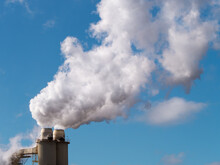 Plumes Of Steam Rising From Industrial Chimneys Into A Blue Sky
