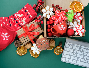 Wall Mural - gift box with christmas decor, gingerbread cookies, cup, nuts, orange slices, socks, keyboard on green backdrop. gift idea, online shopping. Christmas holiday concept. festive winter season. top view