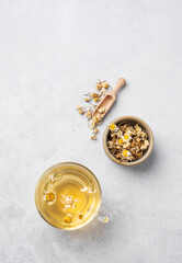 Wall Mural - Chamomile herbal tea in a glass cup on a light background with dry flowers. The concept of a healthy detox drink for health and sleep.