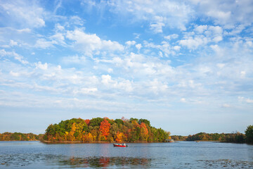 Wall Mural - father and son in fishing boat on a minnesota lake with trees in fall color and beautiful clouds