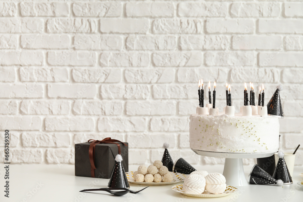 Birthday cake with candles and sweets on white table near brick wall
