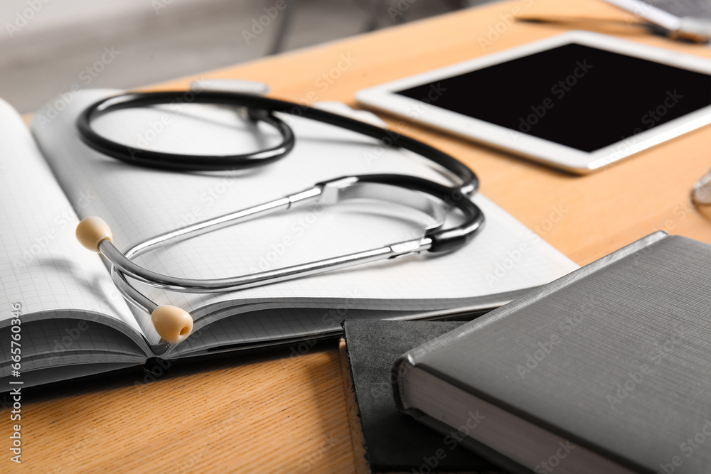 Stethoscope with notebook on wooden medical desk, closeup