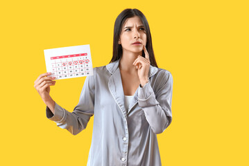 Wall Mural - Thoughtful young woman with menstrual calendar on yellow background