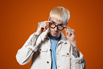 Wall Mural - Young tattooed man in stylish eyeglasses on color background