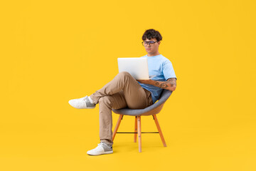 Poster - Male programmer with laptop sitting in chair on yellow background