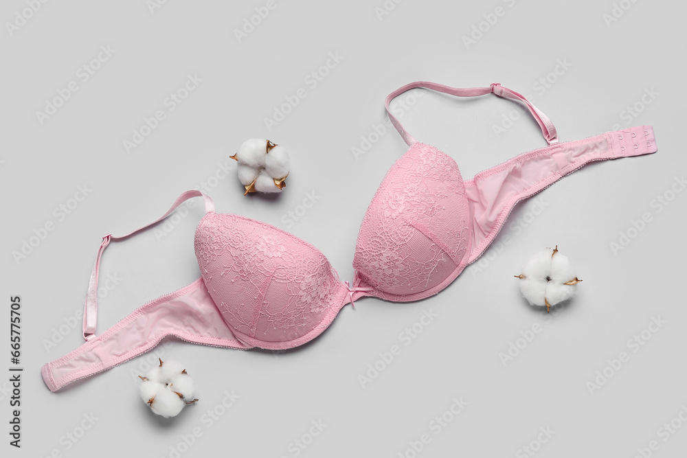 Pink female bra and cotton flowers on grey background
