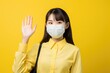 young asian woman in medical mask giving high five on yellow background. coronavirus protection and prevention concept