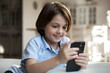 © fizkes - Close up smiling Caucasian boy using smartphone at home, sitting on couch alone, curious adorable 7s child kid looking at phone screen, playing games or watching cartoons, video, leisure time