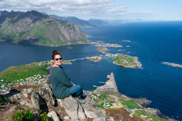 Happy woman hiker enjoys the panorama of lofoten islands at the top of Reinebringen. traveler alone on cliff edge in Norway lifestyle exploring concept. Hike above Reine village in the Lofoten