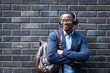 © littlewolf1989 - Portrait of trendy handsome man in business suit and headphones standing by dark brick wall.